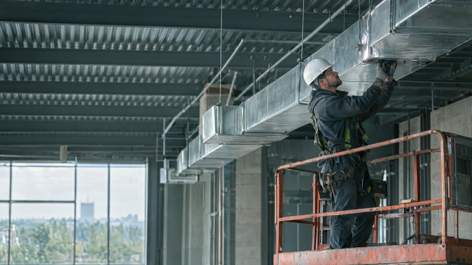 Mechanical contractor installing ceiling ductwork from a lift
